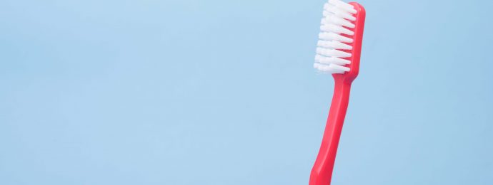 red toothbrush held in front of a solid blue background