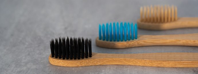 wooden toothbrushes, one with black bristles, one with blue bristles and one with beige bristles